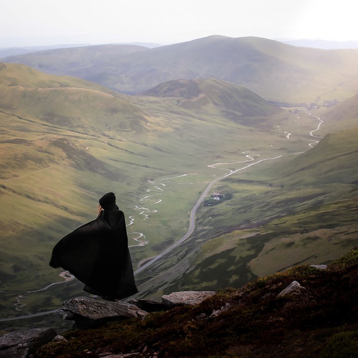 A black caped figure overlooking the beautiful Scottish countryside.