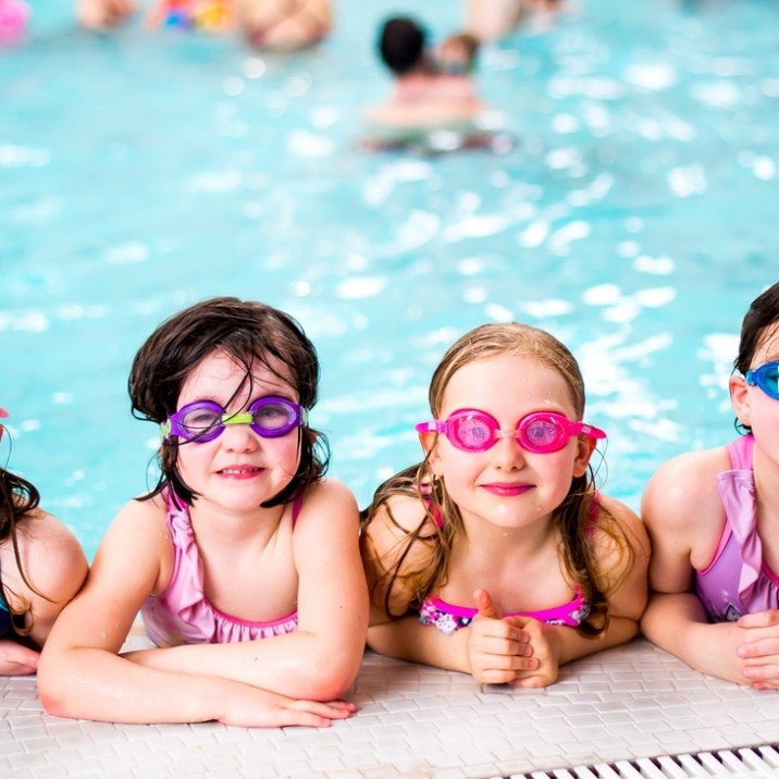 Girls with their goggles on having a break from all the fun at the edge of the pool.